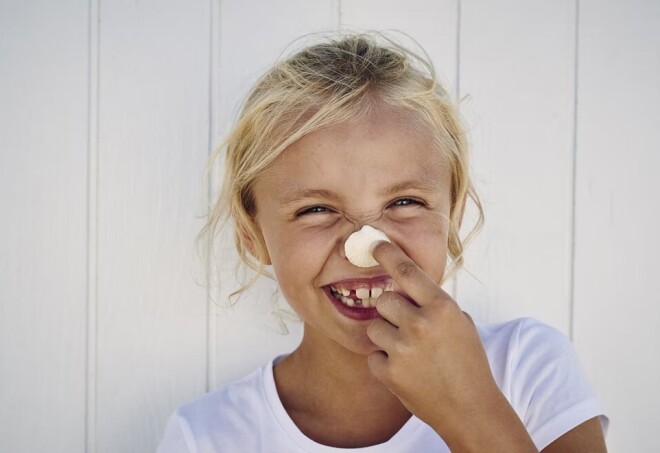 A young girl holds a seashell to her nose