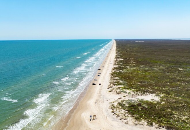 A bird's eye view of a long, straight beach in Corpus Christi, Texas.