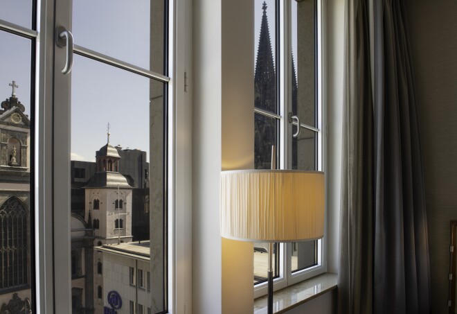 A cream-colored lamp lit in front of a window overlooking historic buildings at Hilton Cologne, Germany