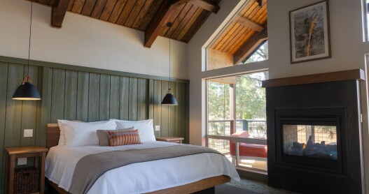 A guest room at Firefall Ranch featuring a bed next to a fireplace and soaring windows