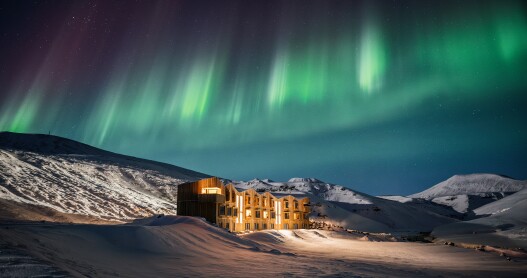 Hotel building with three stories in the middle of a snowy landscape with the northern lights overhead